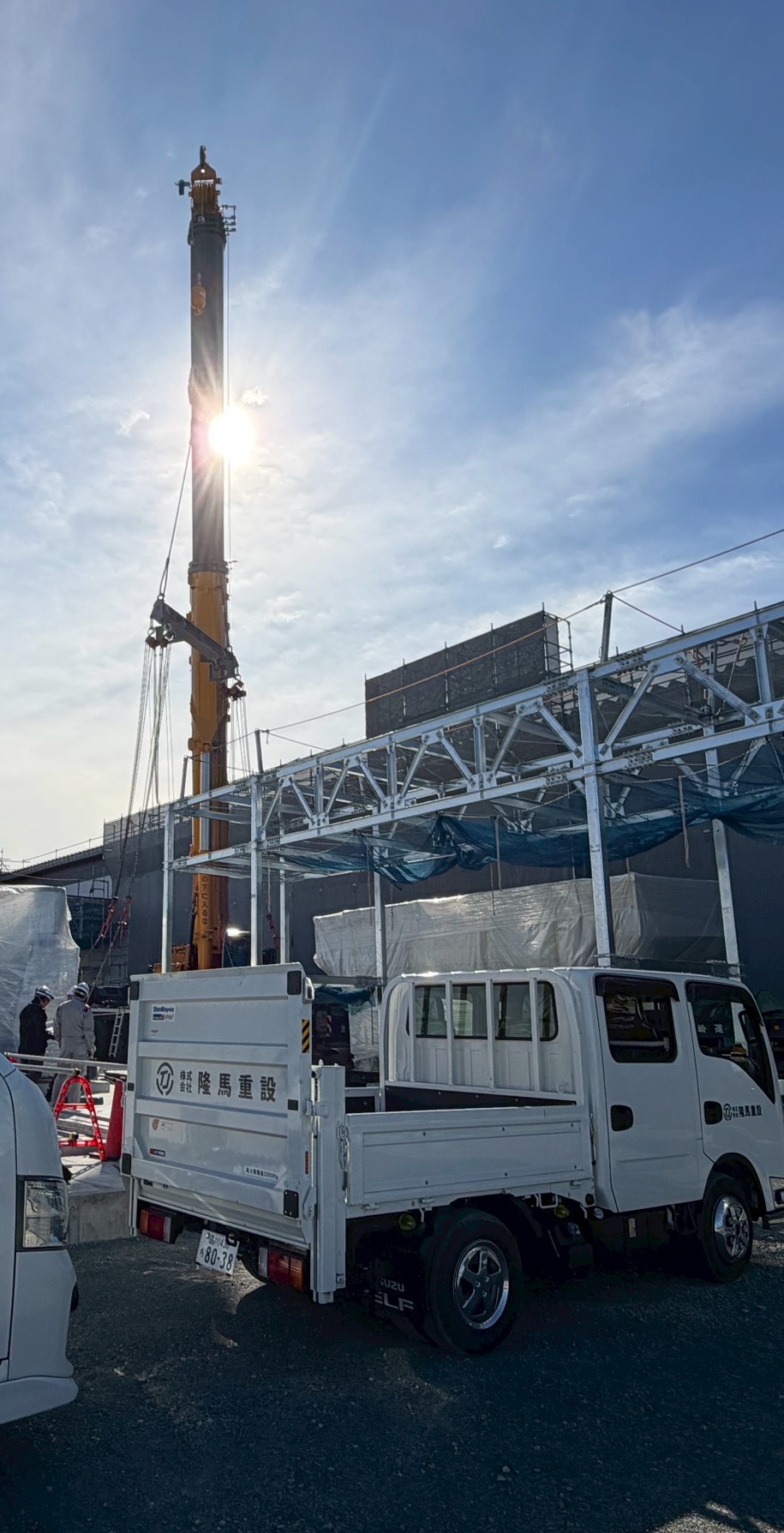 クレーンのある建設現場と社用車